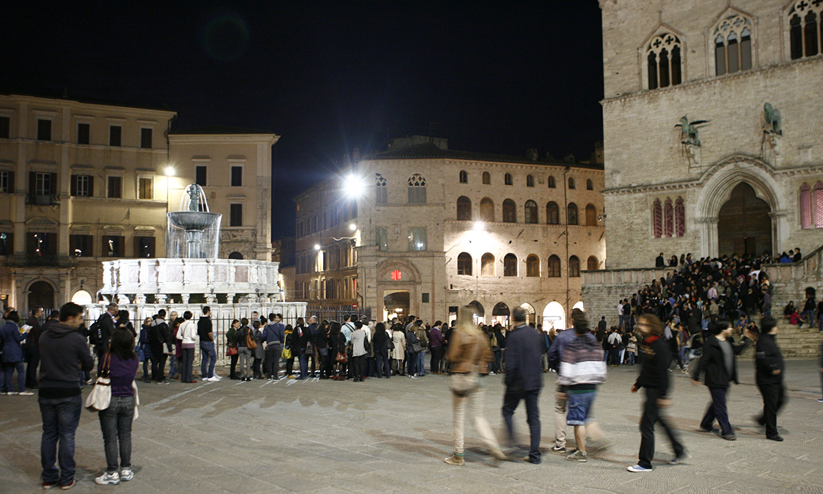 Scorso serale di Piazza IV novembre, a Perugia, con passanti e persone in fila fuori da Palazzo dei Priori